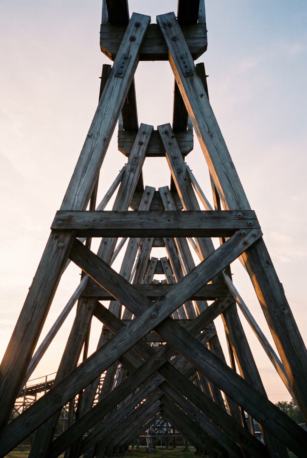 Looking up at a single A-frame timber bent from below, its raking legs and cross-braces converging against a pale dawn sky.