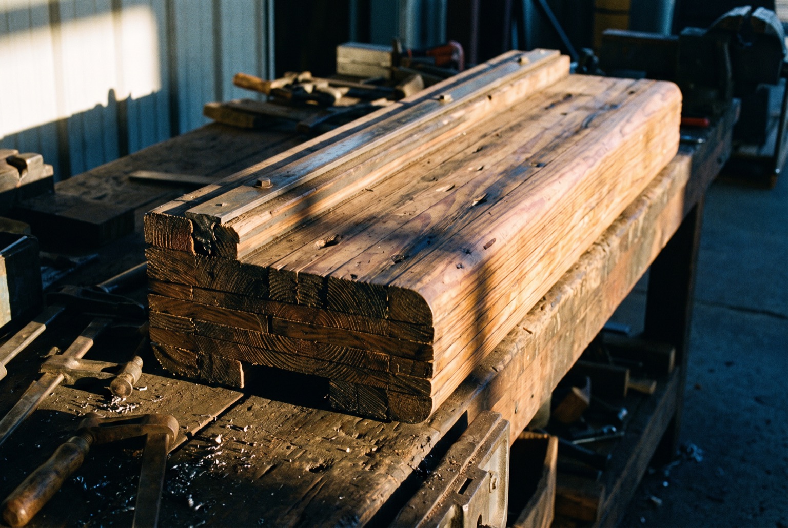 A cut section of laminated coaster track lying on a workbench in daylight, its pine layers visible at the sawn end, the steel running rail still bolted on top.