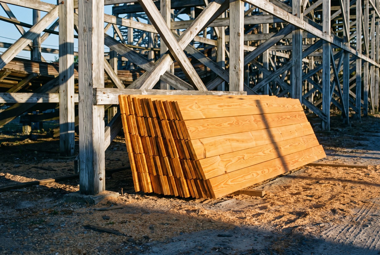 A stack of newly milled bright gold southern yellow pine boards leaning against the weathered grey legs of a coaster structure.